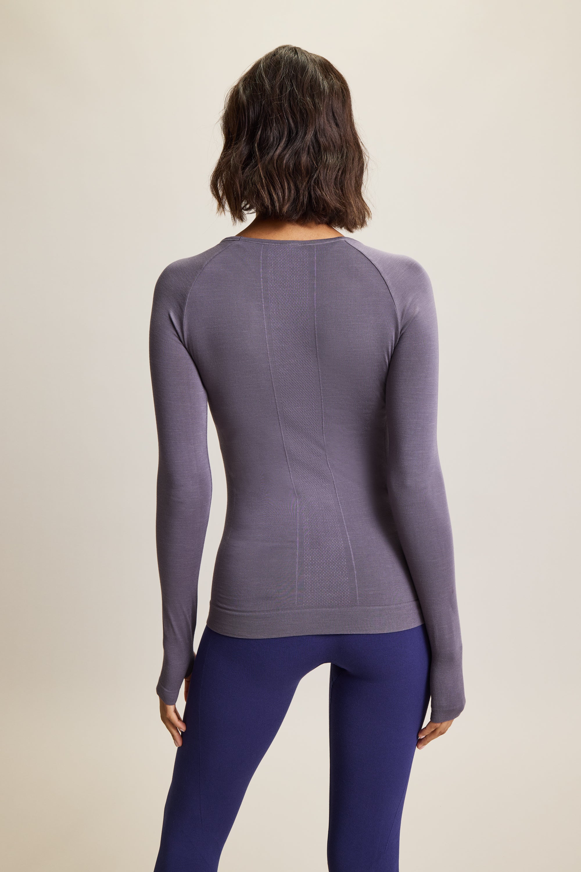 Model wearing a grey long-sleeve top made from moisture-wicking fabric, paired with high-waisted green leggings. The sleek, seamless design of the lightweight and breathable long-sleeve top, featuring thumbholes, makes it perfect for yoga and athleisure wear. Ideal for activewear enthusiasts seeking stylish and sustainable workout gear, this outfit combines high-performance sportswear with versatile, all-day comfort. Suitable for a variety of activities, from intense workouts to casual athleisure looks