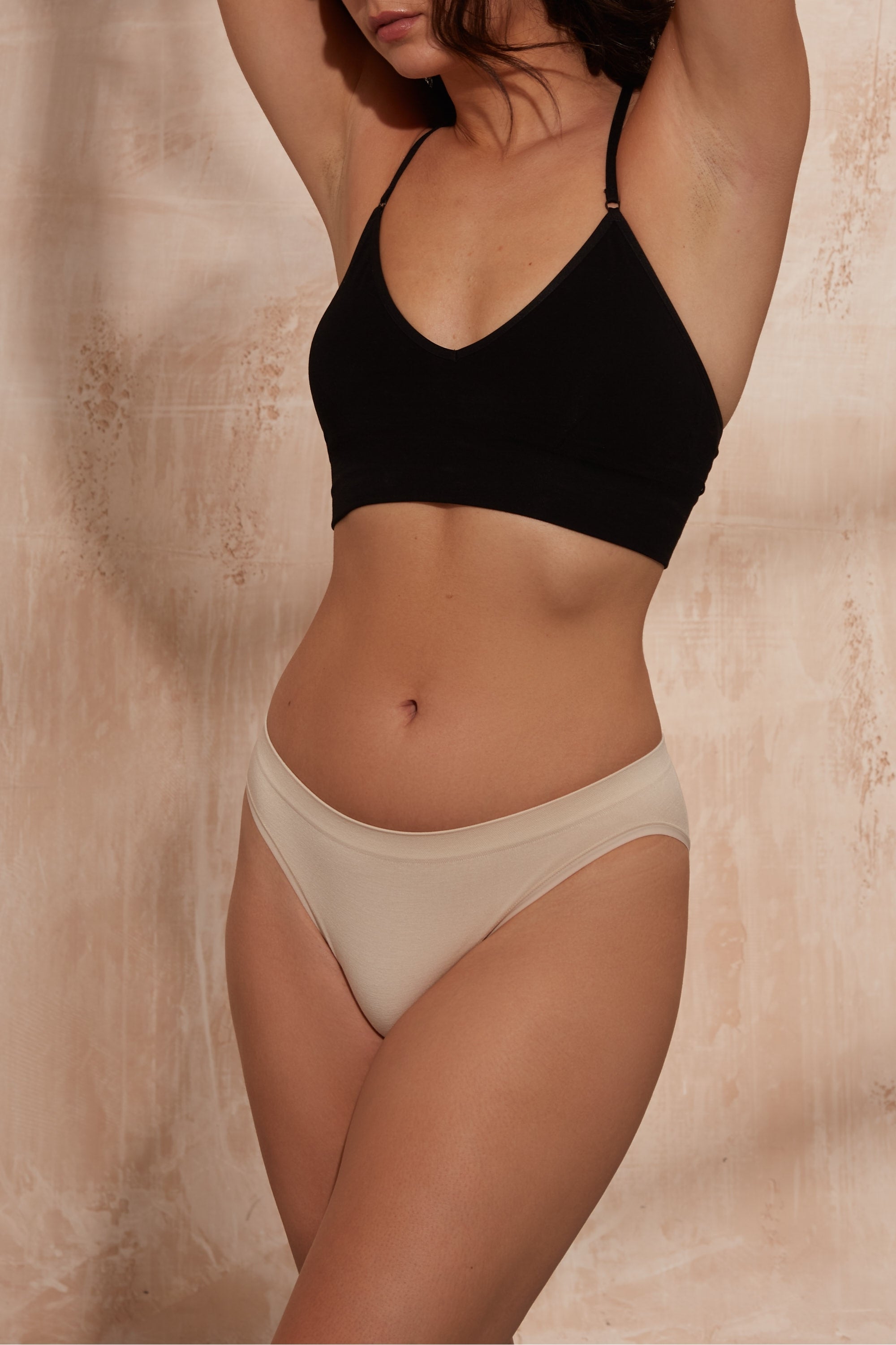 Model wearing black top and beige briefs.