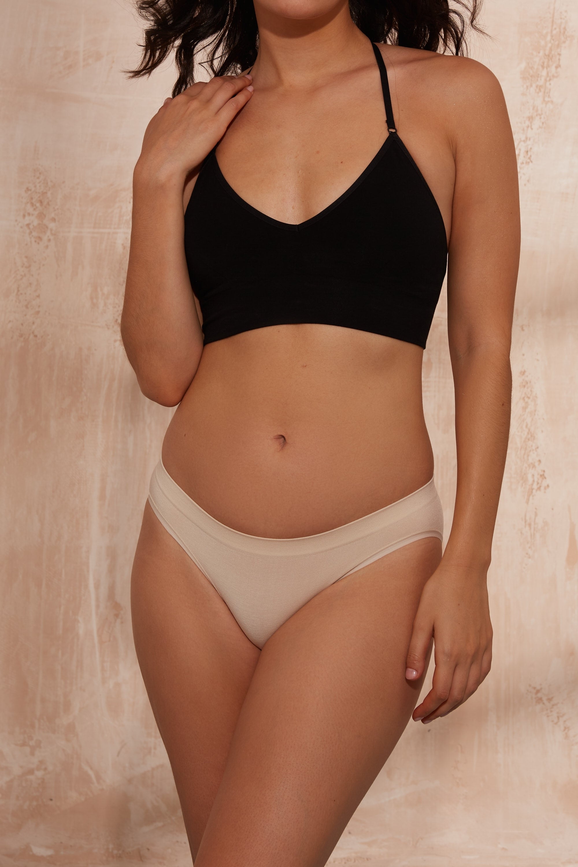 Model wearing black top and beige briefs.